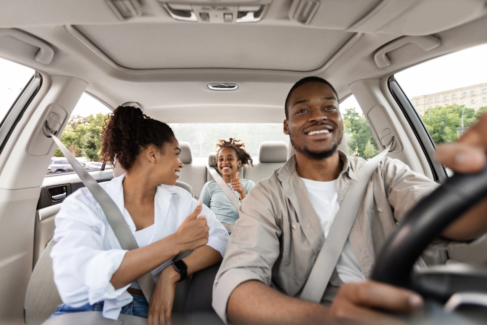 Happy family of three driving in the car safely with seatbelts on